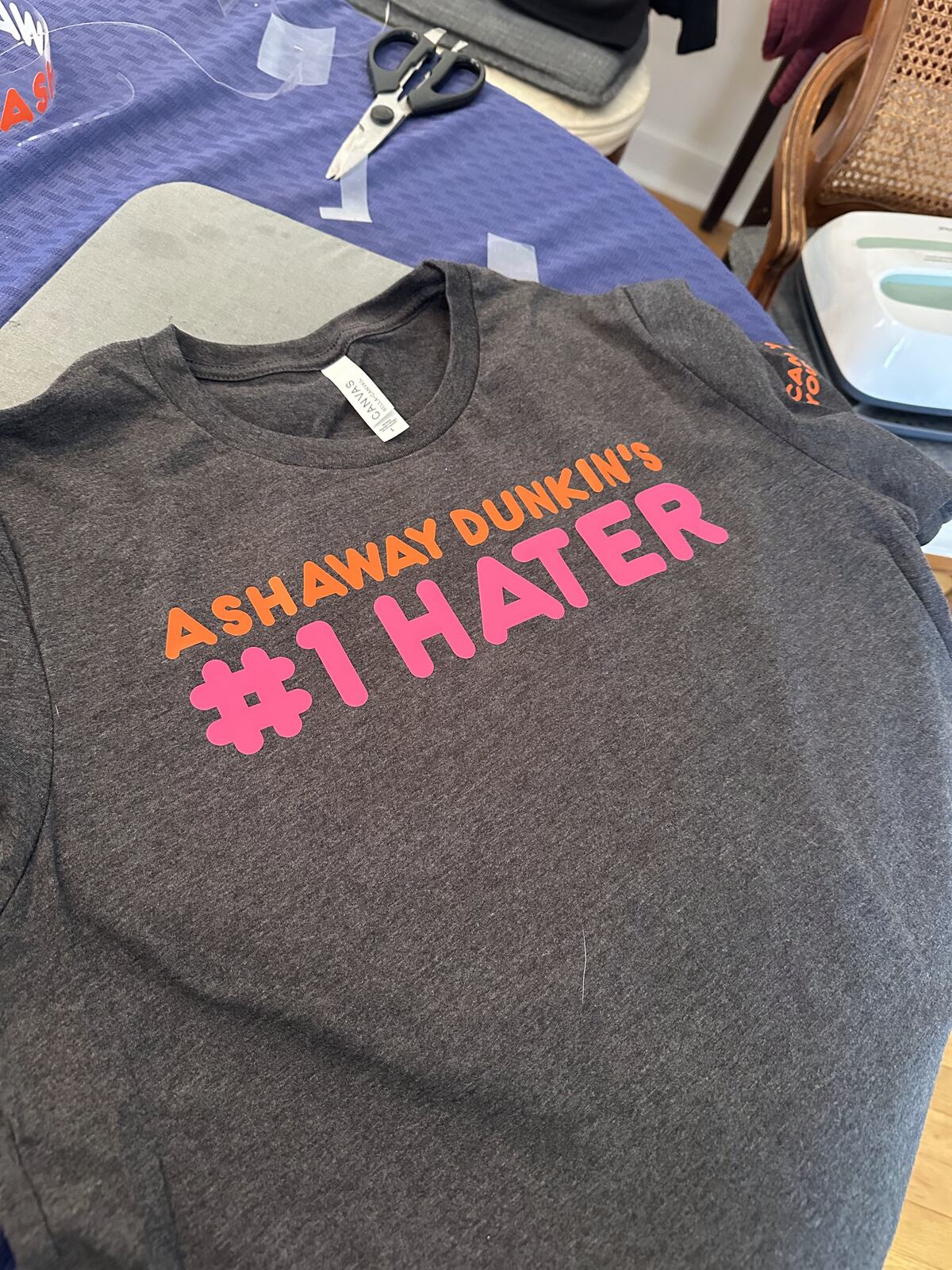 A grey t-shirt with a pink and orange local joke printed on the chest