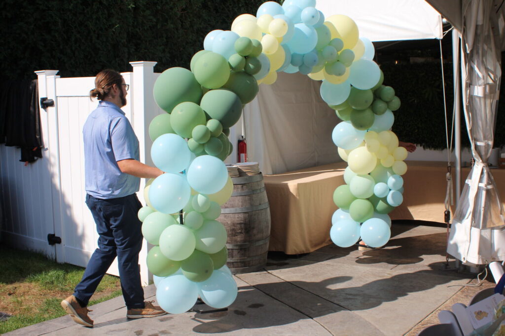 A green and blue balloon arch being installed under an event tent