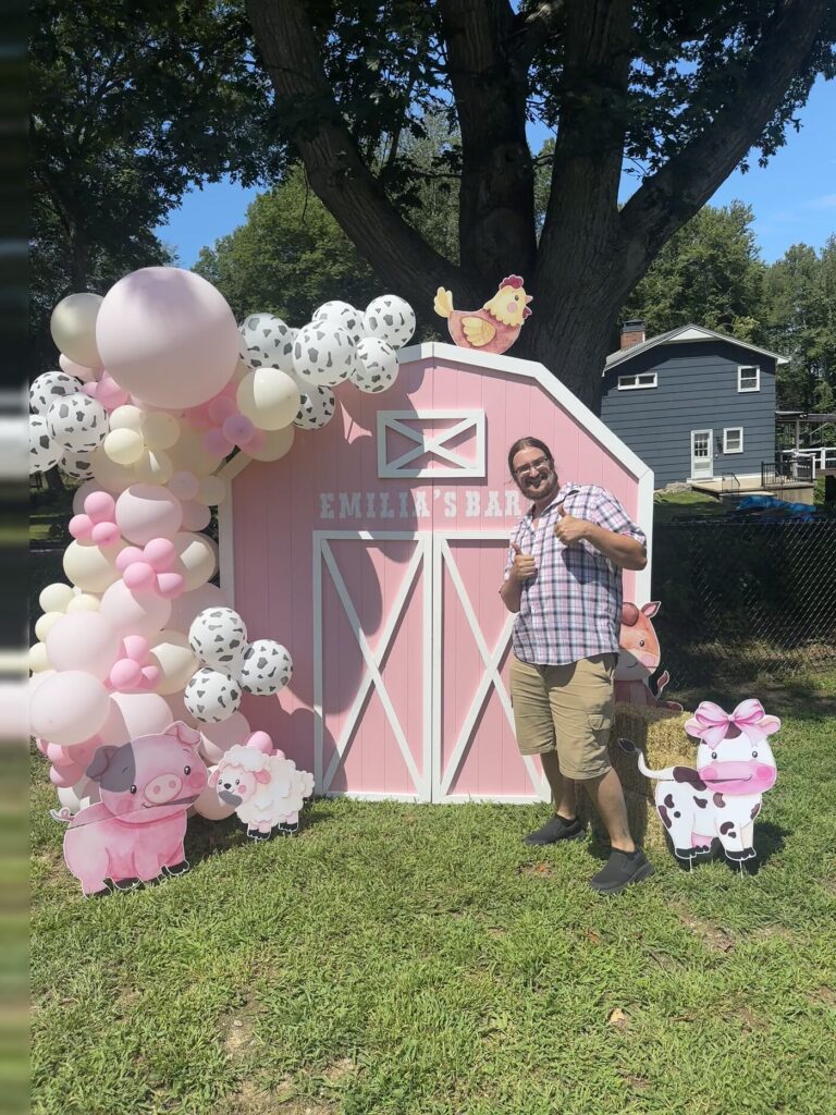 Dylan standing beside the pink barn backdrop with one arm raised, showing how tall the barn is