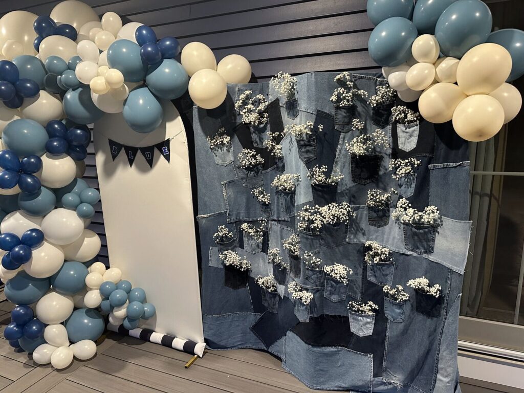 A denim backdrop and blue balloon garland for a baby shower