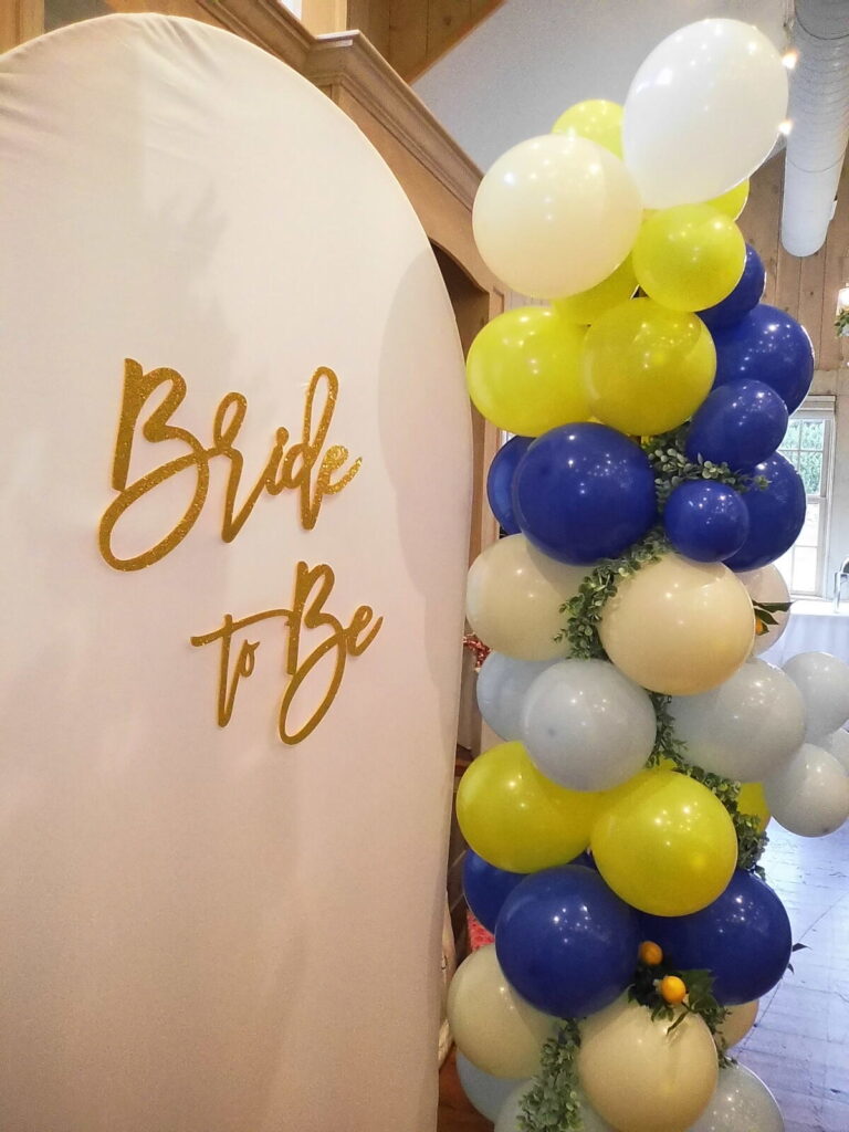 A balloon column in navy, yellow and cream beside a Bride To Be backdrop