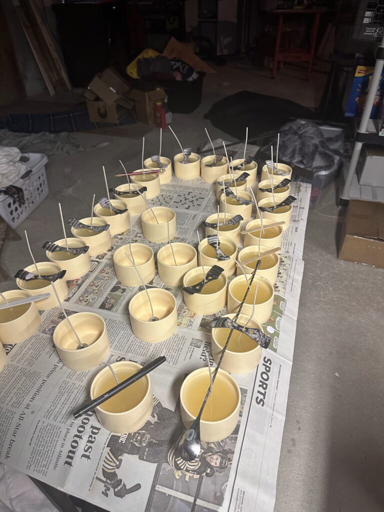 Rows of freshly poured candle tins cooling on a newspaper-covered table