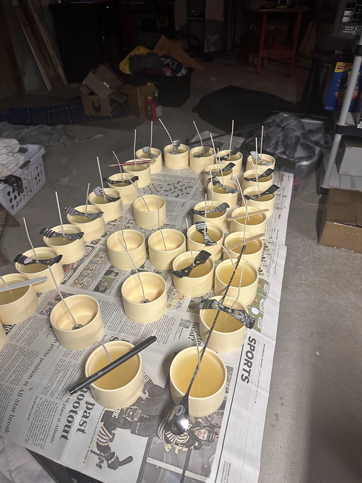Rows of freshly poured candle tins cooling on a newspaper-covered table
