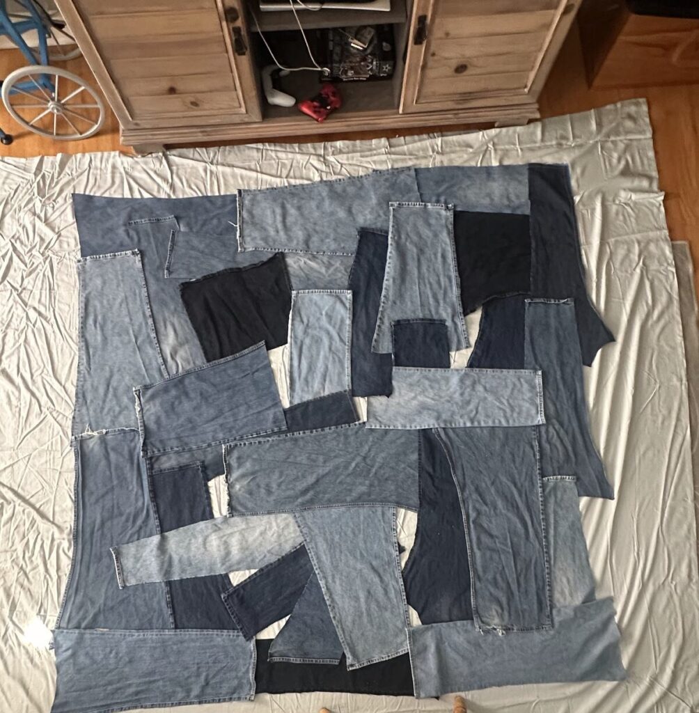 Squares cut from old jeans laid out as a patchwork on a white sheet on the floor, seen from above, before they are sewn together