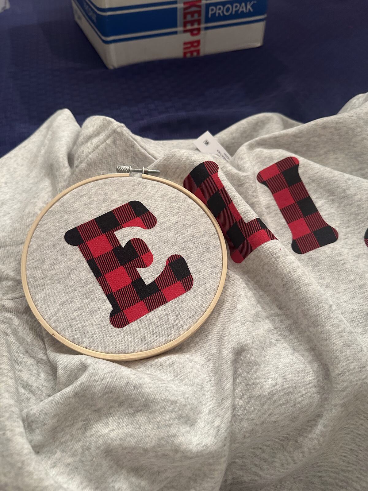 Buffalo plaid fabric letters being appliqued onto a sweatshirt in an embroidery hoop