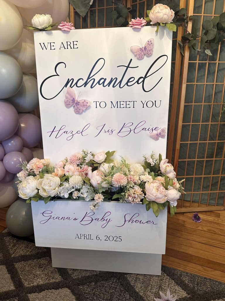 A baby shower welcome sign with butterflies, flowers and a pastel balloon garland