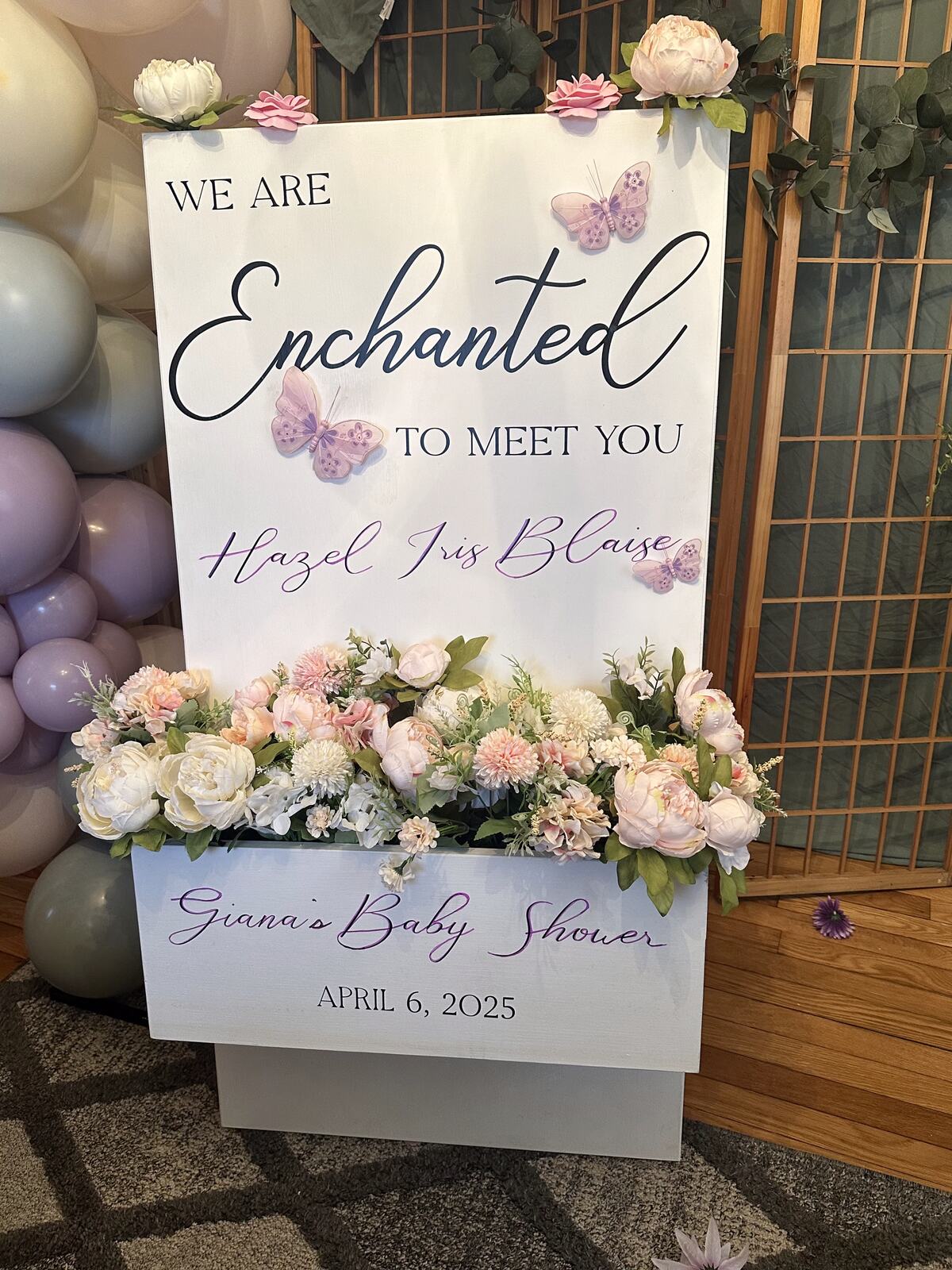 A baby shower welcome sign with butterflies, flowers and a pastel balloon garland