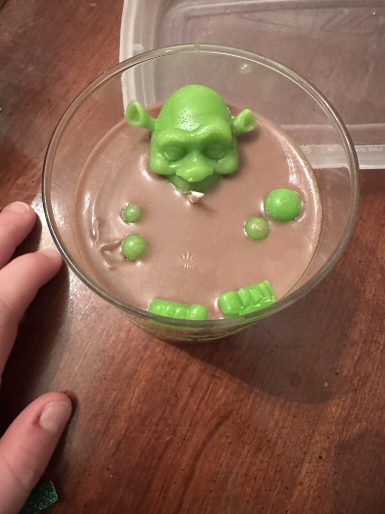 A green wax candle shaped like an ogre in a swamp, set in a glass