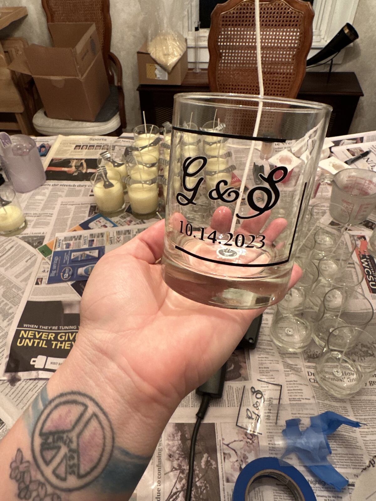 A hand holding an etched glass candle over a newspaper-covered worktable