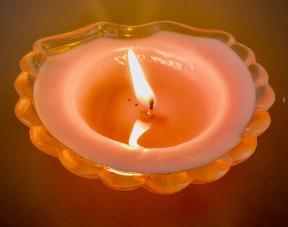 A candle burning low in a scalloped glass dish