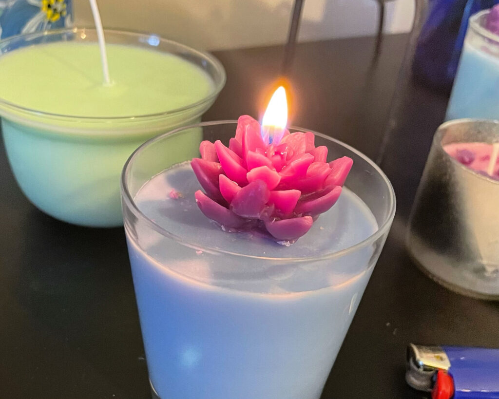 A lotus-shaped candle lit and floating in a wide vessel