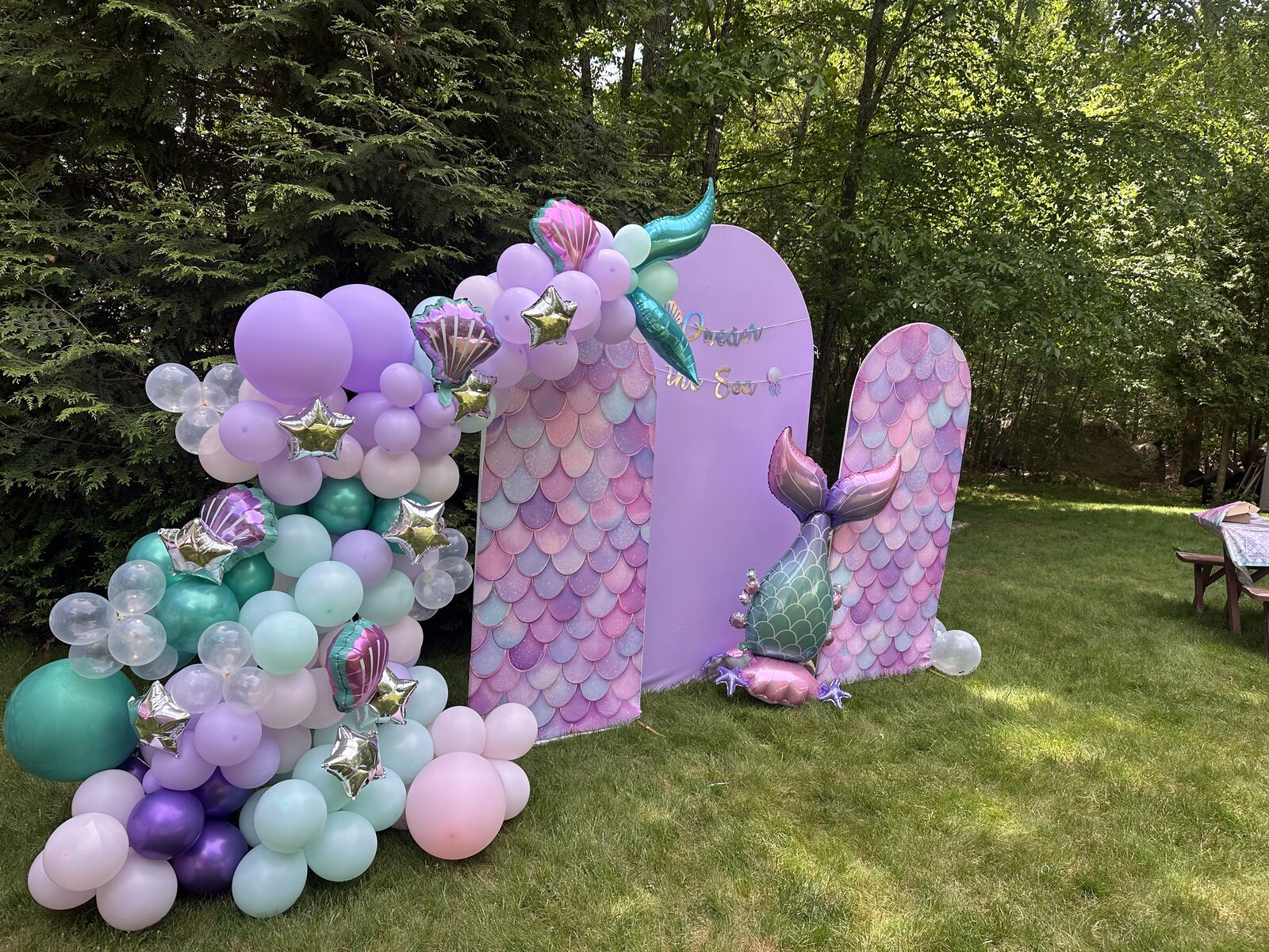 A mermaid-themed backdrop with a pastel balloon garland on a lawn