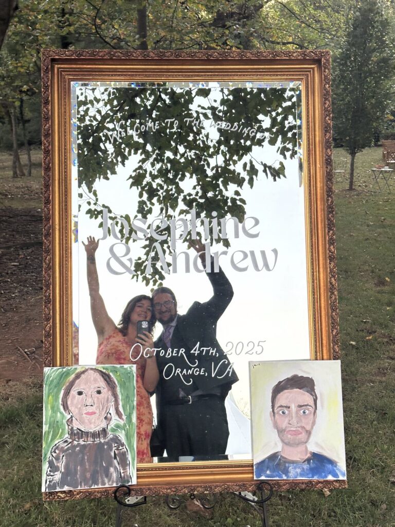 A mirror welcome sign flanked by painted portrait cutouts of the couple