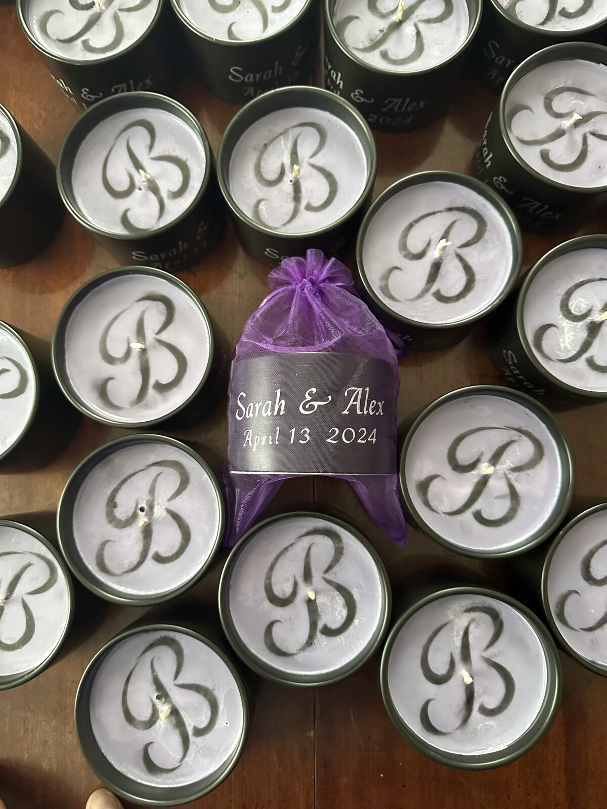 Monogrammed candle tins beside an organza favour bag printed with names and a date