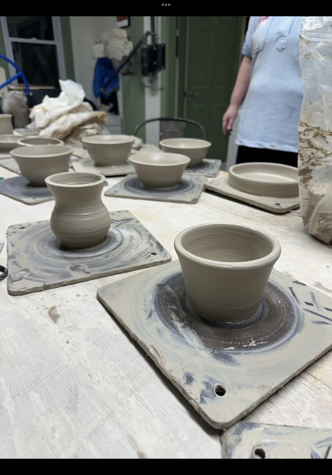 Thrown pots drying on boards beside a pottery wheel