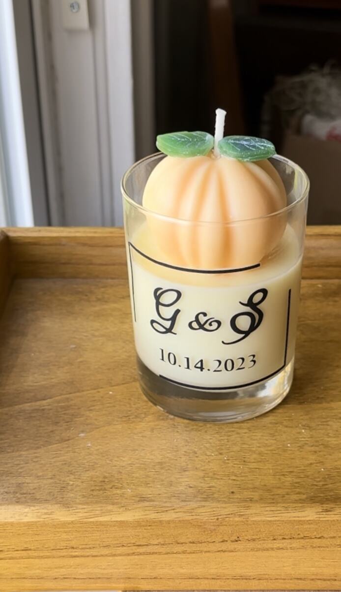 A pumpkin-shaped candle in a glass vessel with a monogram label
