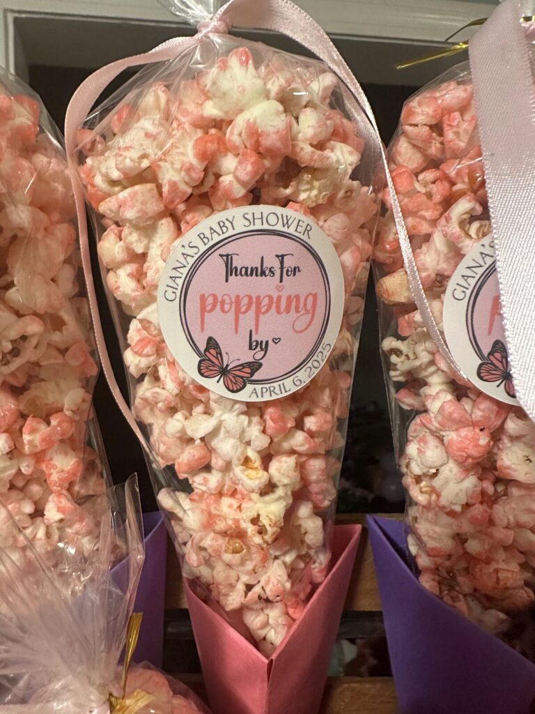 Cellophane cones of pink and white popcorn tied with pink ribbon, each carrying a round printed label