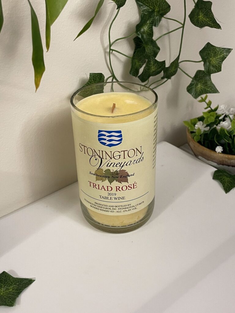 A candle poured into a cut-down wine bottle that still carries its original winery label, with ivy trailing behind it